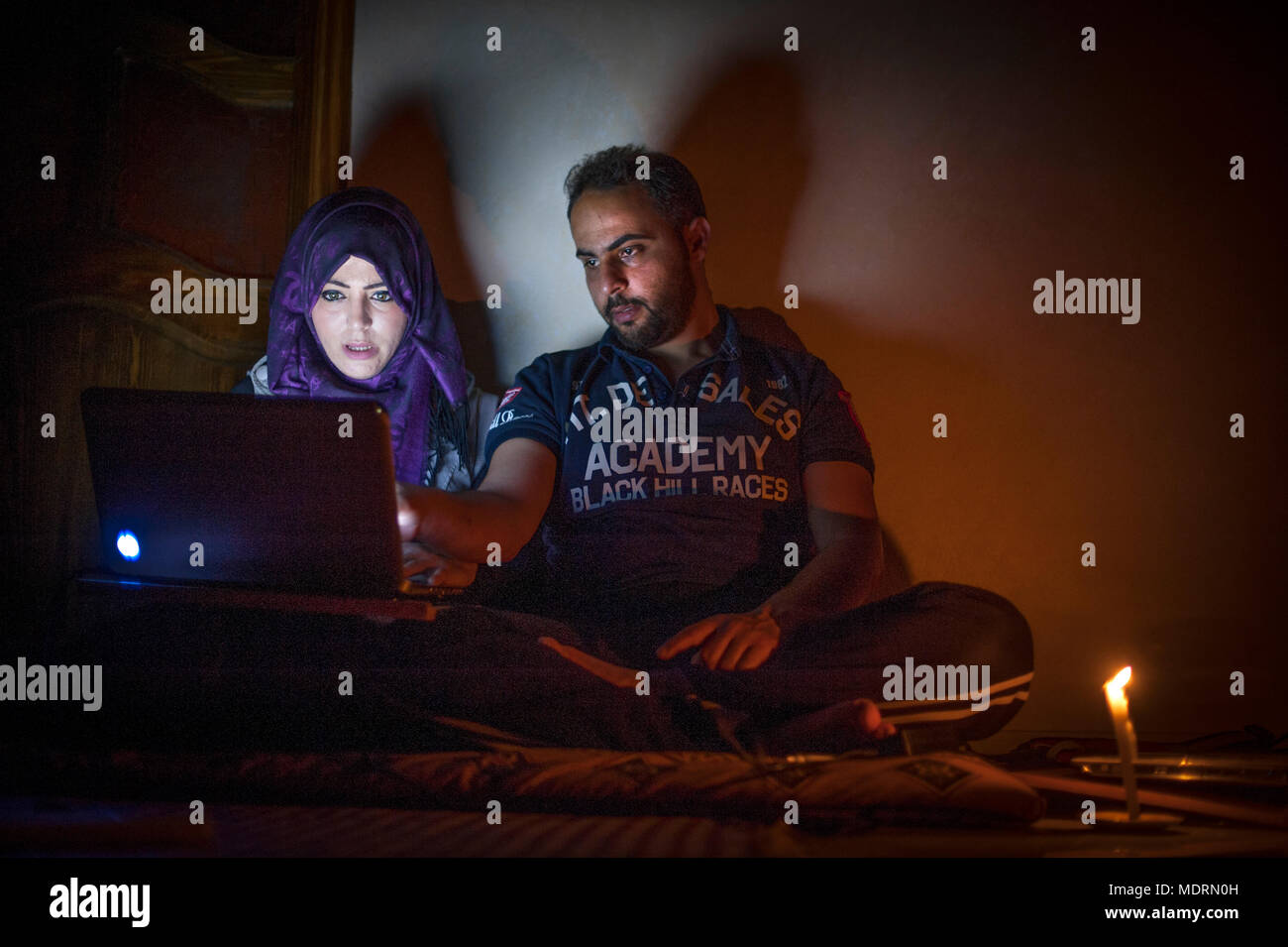 IT specialists Mohammad and Tala Al-Nagi try to work at home through a power cut in Gaza with the remaining battery in their lap top computers. Stock Photo