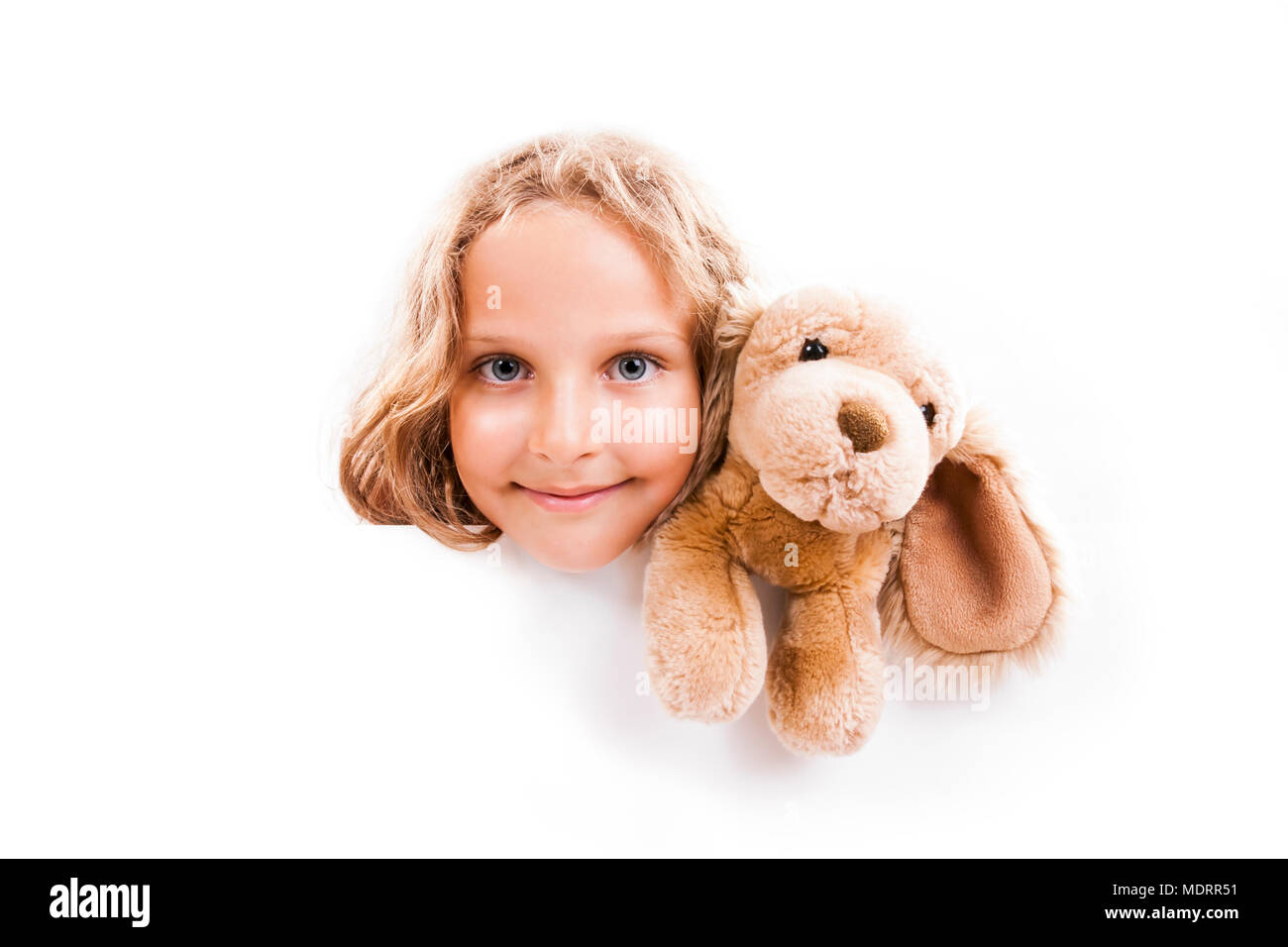 Smiling 7 years old girl with cuddly dog looks out from the empty banner with space for text, isolated on white. Stock Photo