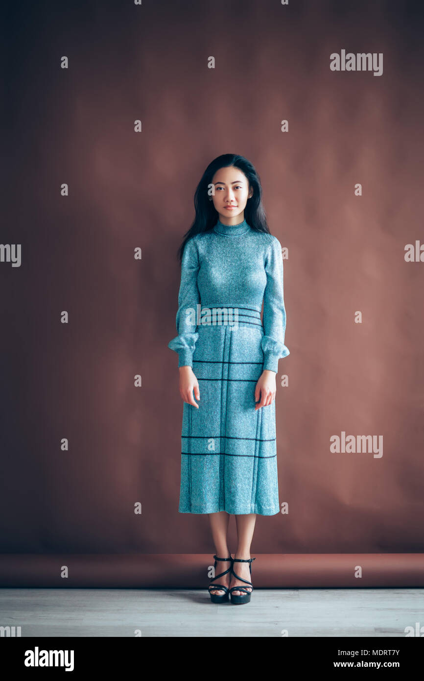 Full length portrait of beautiful asian girl in blue dress on brown ...