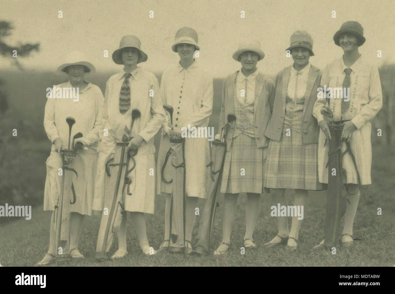 Golfers at the links in Atherton ca 1925. Location:   Atherton, Queensland  Description: Young women wearing cloche hats, skirts and jackets. Each has her own set of golf clubs. Stock Photo
