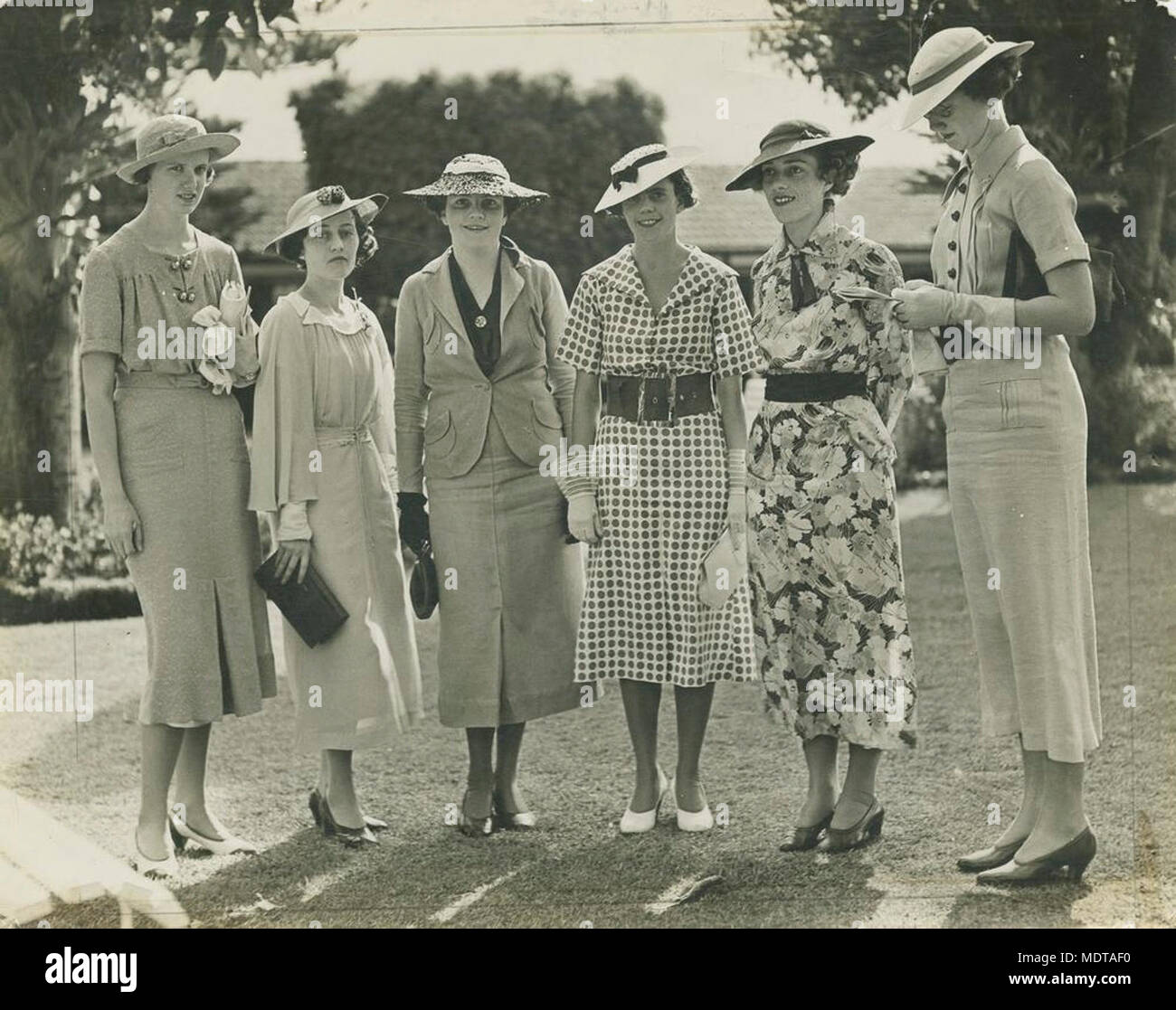 Group of ladies enjoying a day out at the races,. Location:  Brisbane, Queensland, Australia  Date:  Undated  Description:  Six ladies, all wearing smart dresses and wide-brimmed hats, are gathered on the lawn at the races. Stock Photo