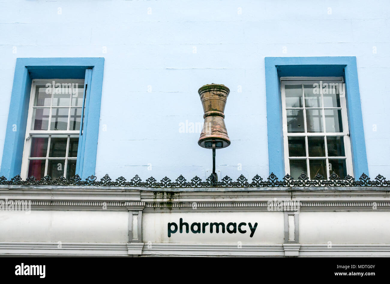 Old fashioned apothecary sign of gold mortar above pharmacy shop doorway against a blue wall and windows, High Street Haddington, Scotland, UK Stock Photo