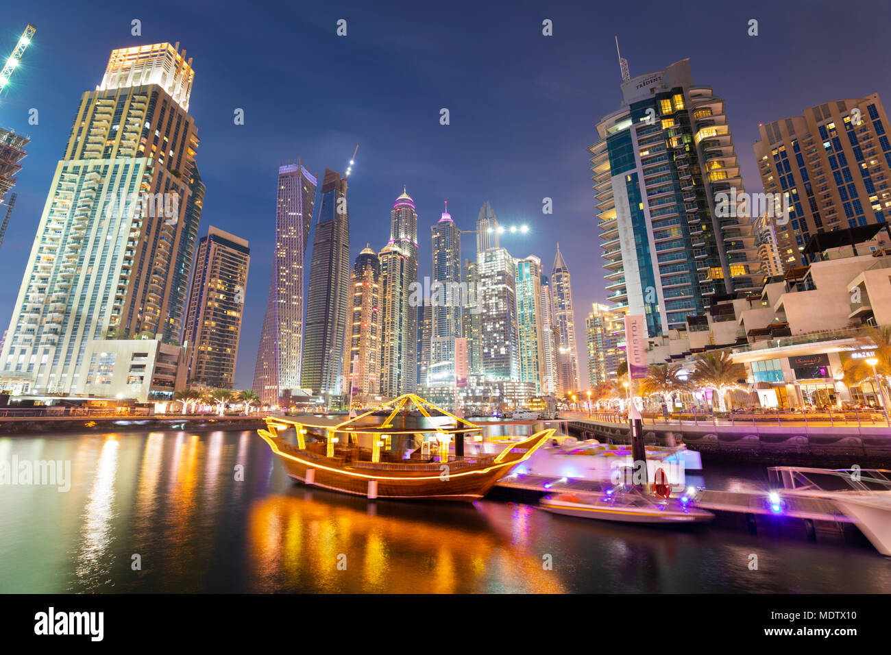 Modern architecture with sightseeing dhow below towers lit up at night in the Dubai Marina, Dubai, United Arab Emirates, Middle East Stock Photo