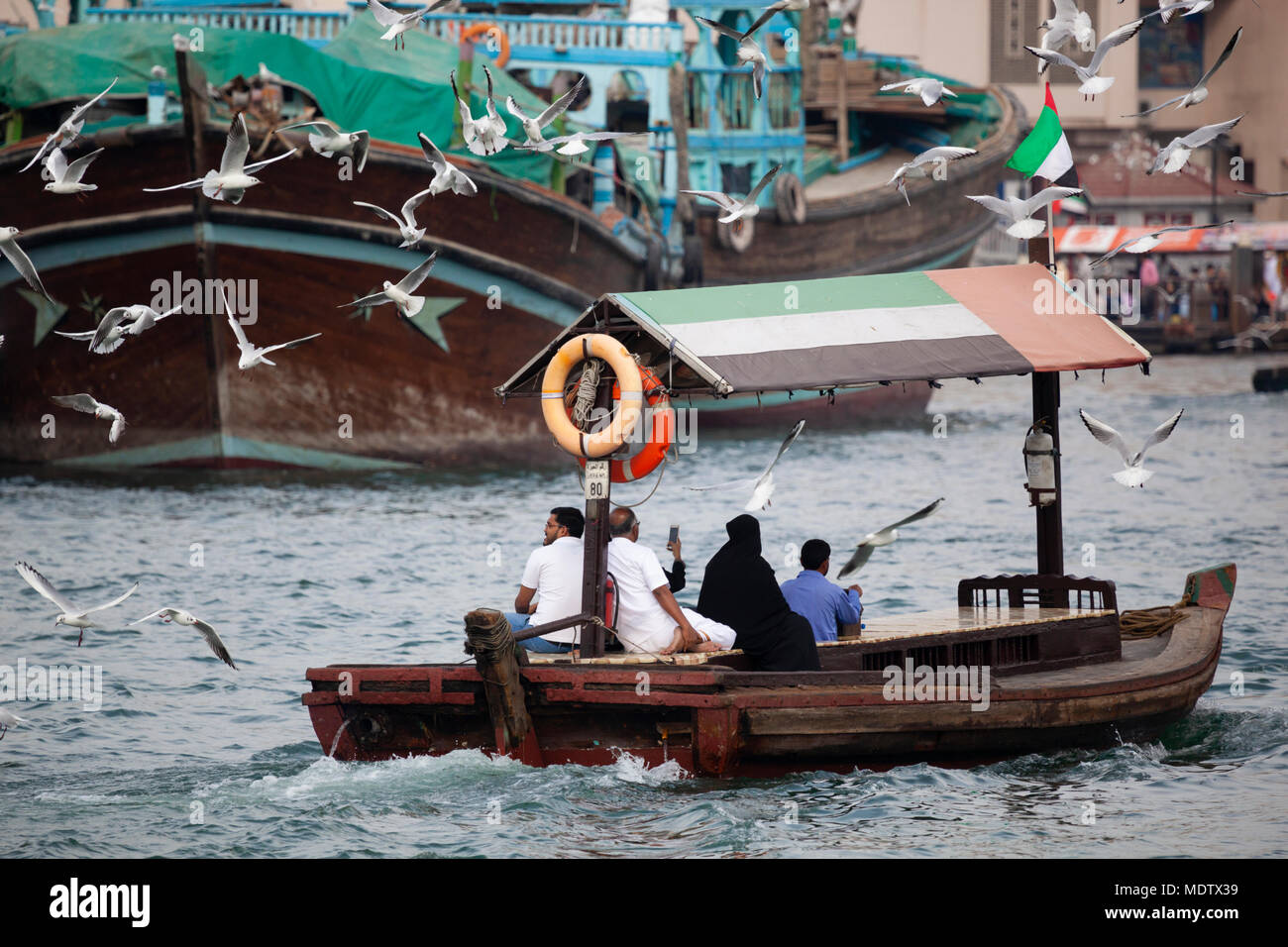 Local people crossing the Dubai Creek on an abra with dhows in the background and seagulls flying behind, Dubai, United Arab Emirates, Middle East Stock Photo