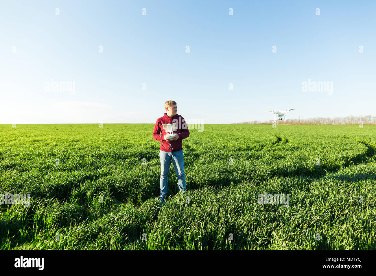 quadcopter outdoors, aerial imagery and recreation concept - male man in jeans and fleece hoodie controls the flight altitude of superb white drone, b Stock Photo