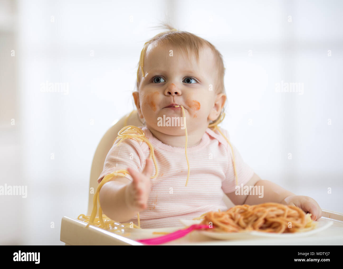 Cute baby toddler girl eating spaghetti with tomato sauce sitting in a