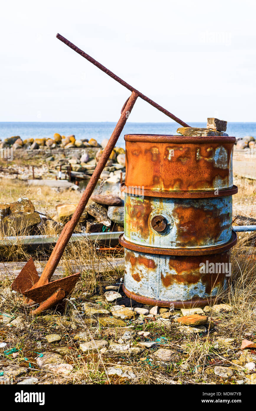 Rusty old barrel with rusty and old anchor in coastal landscape. Barrel used as smoker when smoking fish. Bottom removed and placed over smoke hole or Stock Photo