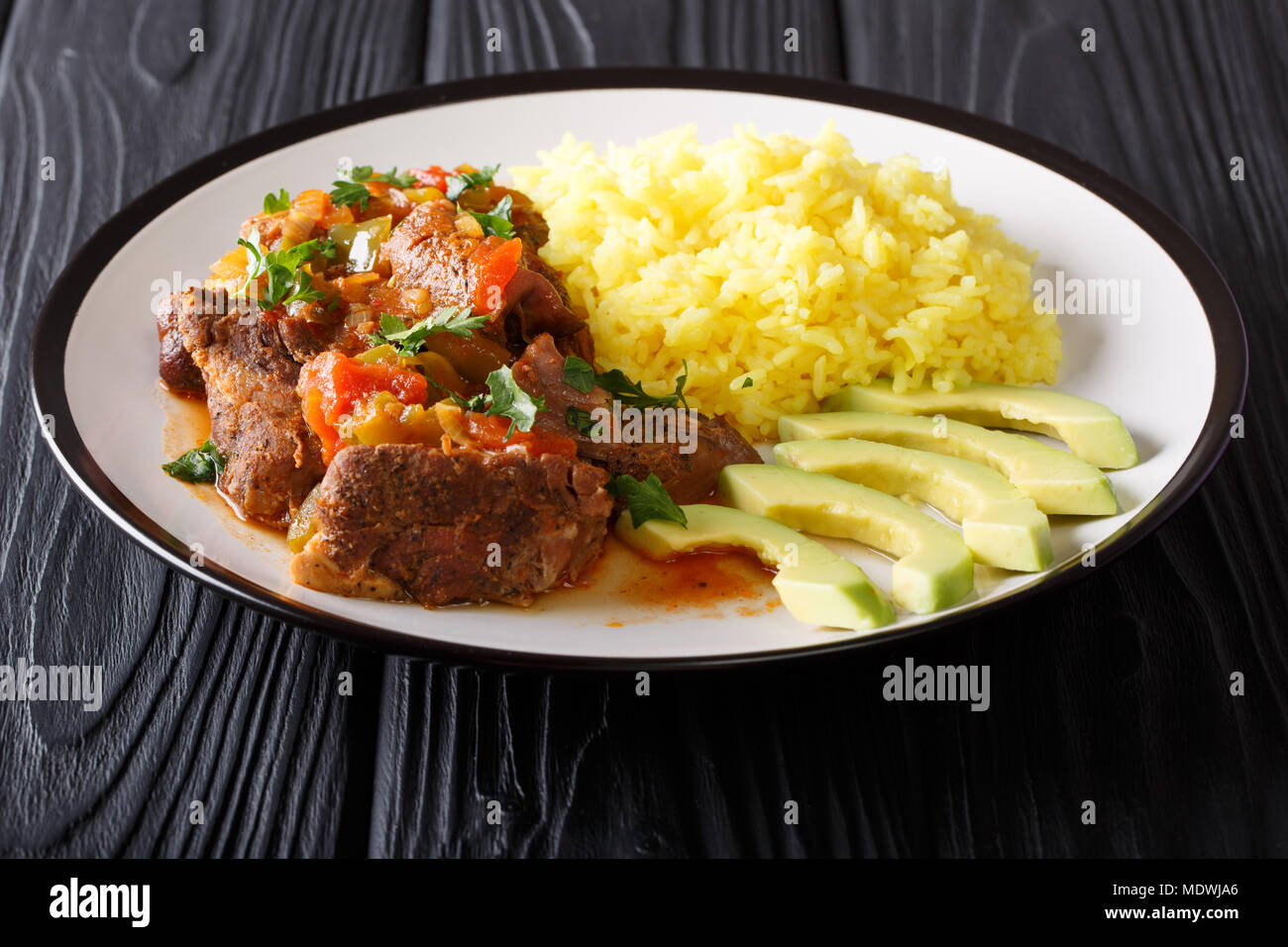 Ecuadorian traditional food: seco de chivo goat meat with a garnish of yellow rice and avocado close-up on a plate on the table. horizontal Stock Photo