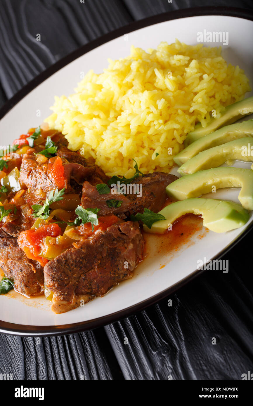 Portion of seco de chivo stewed goat meat with yellow rice and avocado
