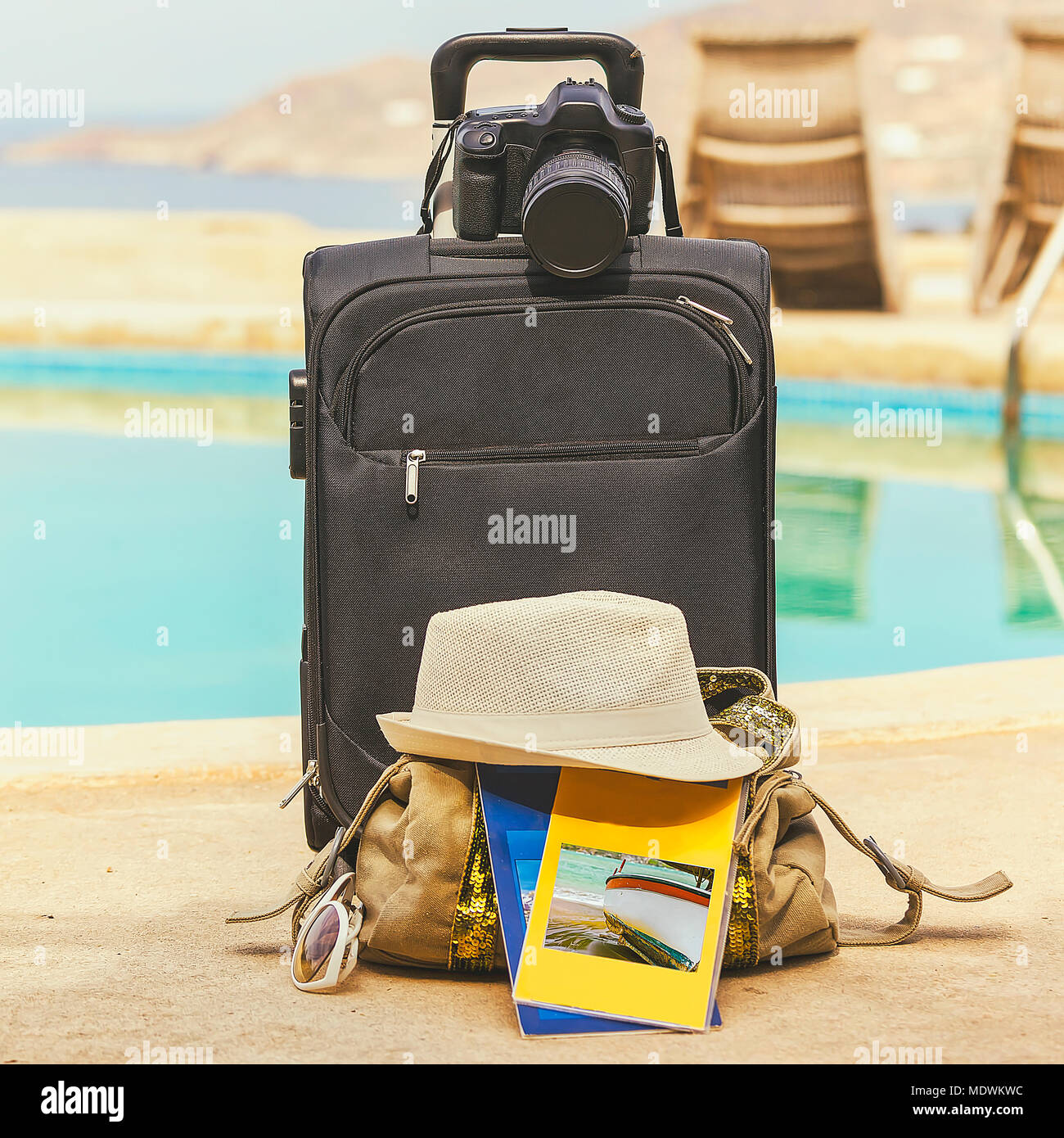 Arrival at holiday destination with black suitcase and dslr. Background swimming pool. Stock Image. Stock Photo