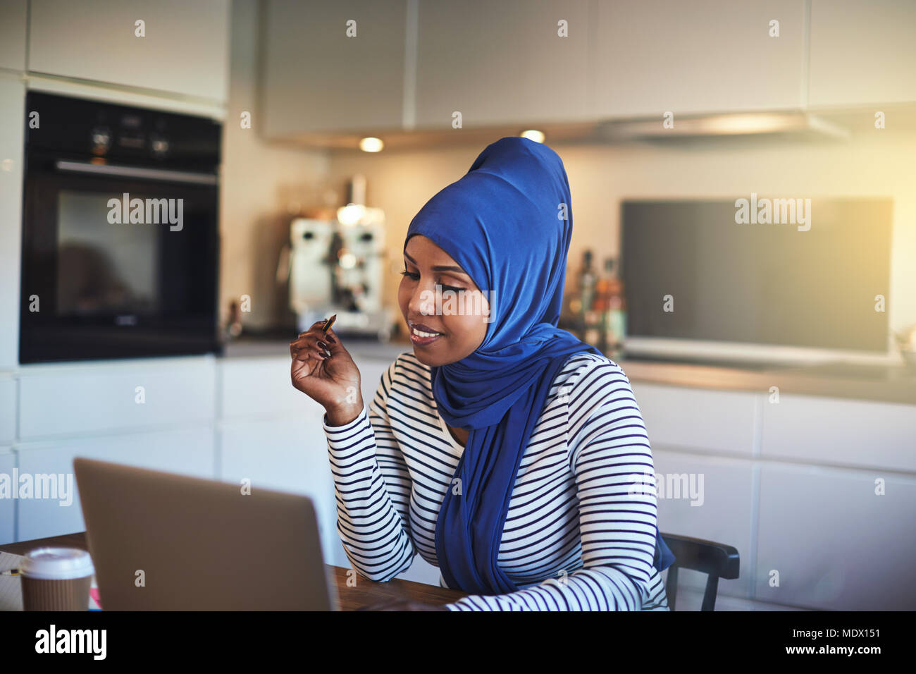 Smiling young Arabic female entrepreneur wearing a hijab sitting at her ...