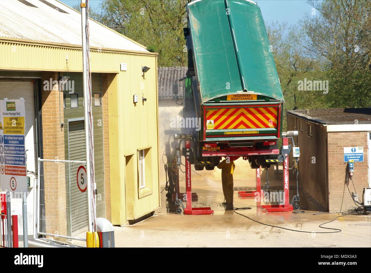 View of a Smiths Bletchingdon lorry on ramp being washed with back of lorry raised on axle with man underneath cleaning Stock Photo