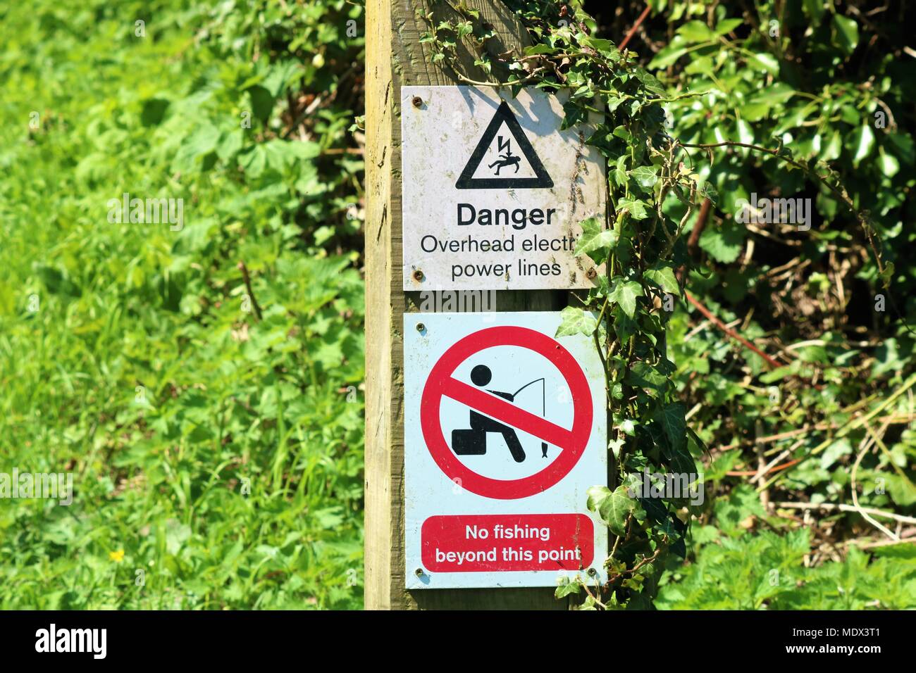Danger - Overhead electric power lines' and 'No fishing beyond this point'  signs on wooden post at side of canal Stock Photo - Alamy