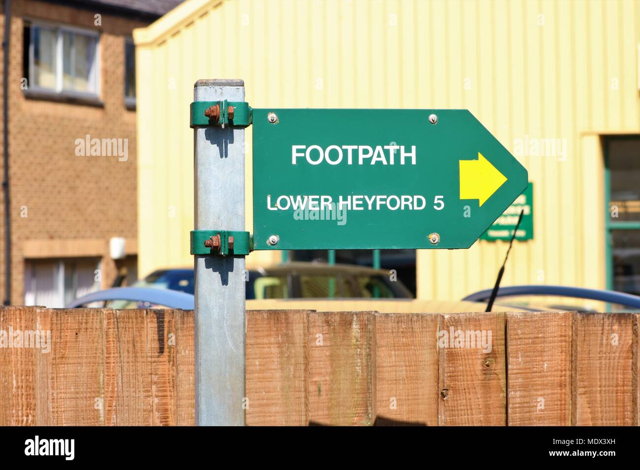 Green signpost at side of canal at Enslow Wharf, Bletchingdon, Oxfordshire, UK 'Footpath Lower Heyford 5' on a metal post with view of fence Stock Photo