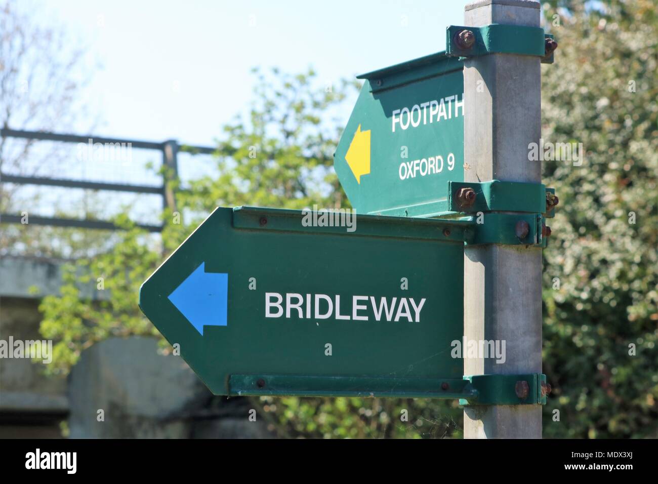 Green signpost at side of canal at Enslow Wharf, Bletchingdon, Oxfordshire, UK 'Footpath Oxford 9 & Bridleway' on a metal post with view of bridge Stock Photo