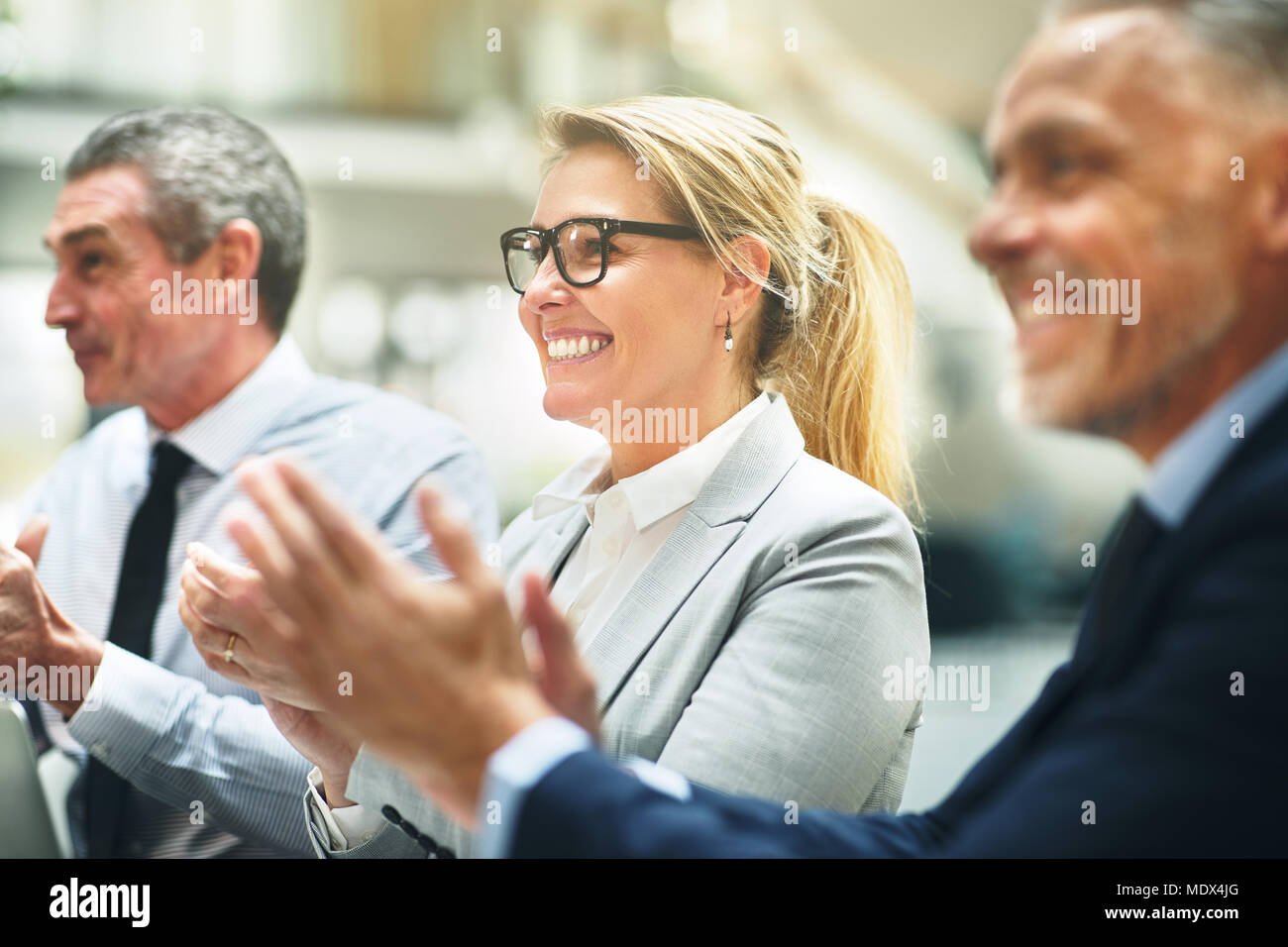 Smiling mature businesswoman clapping hands with two male coworkers while sitting at a table during an office presentation Stock Photo