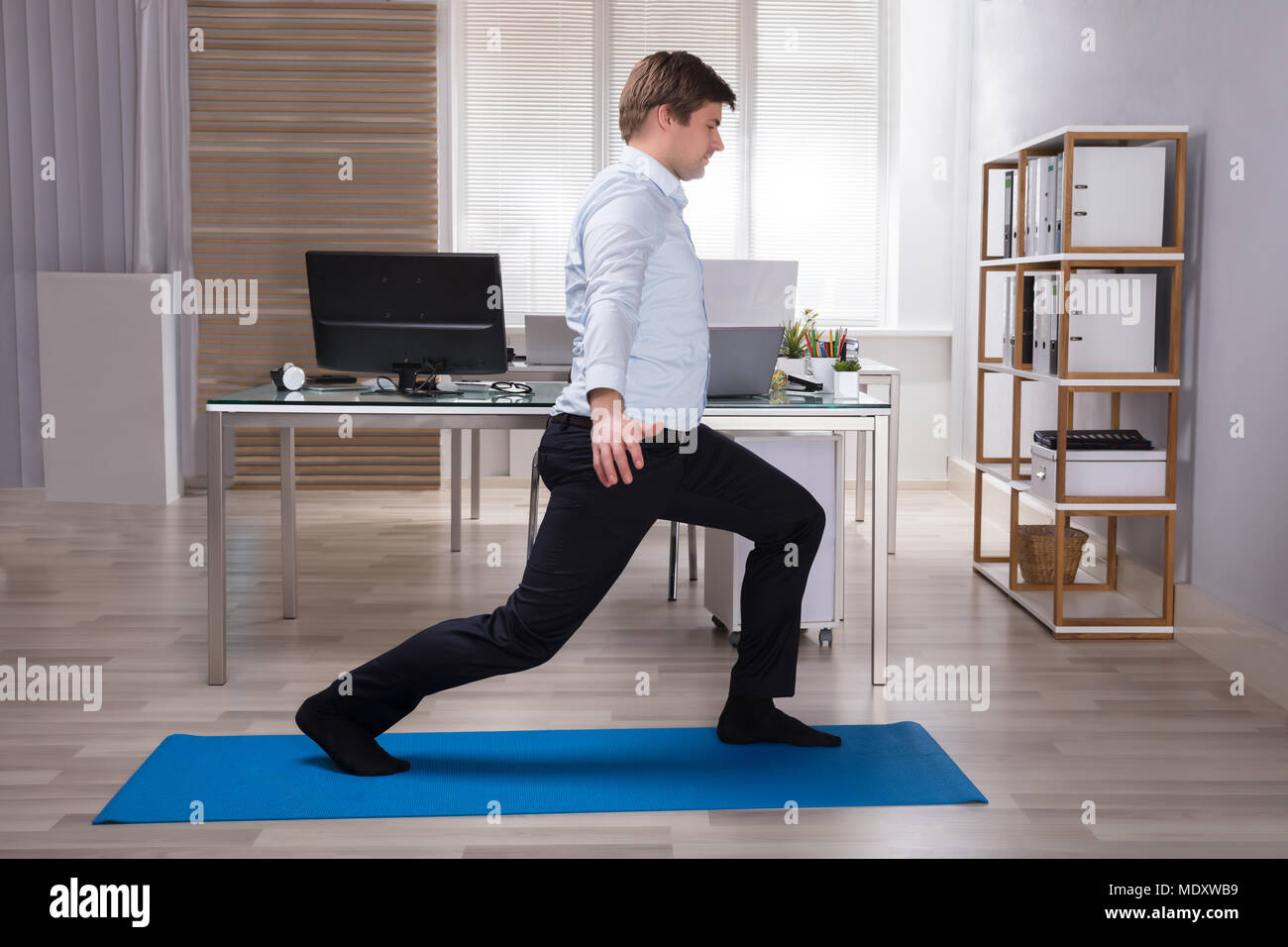 Side View Of A Young Businessman Doing Stretching Exercise On Exercise Mat In Office Stock Photo
