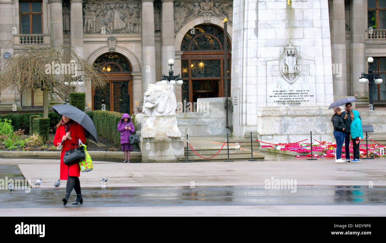 wet and rainy cenotaph war memorial red coat umbrella locals and tourists  in front of city chambers George Square, Glasgow, UK Stock Photo