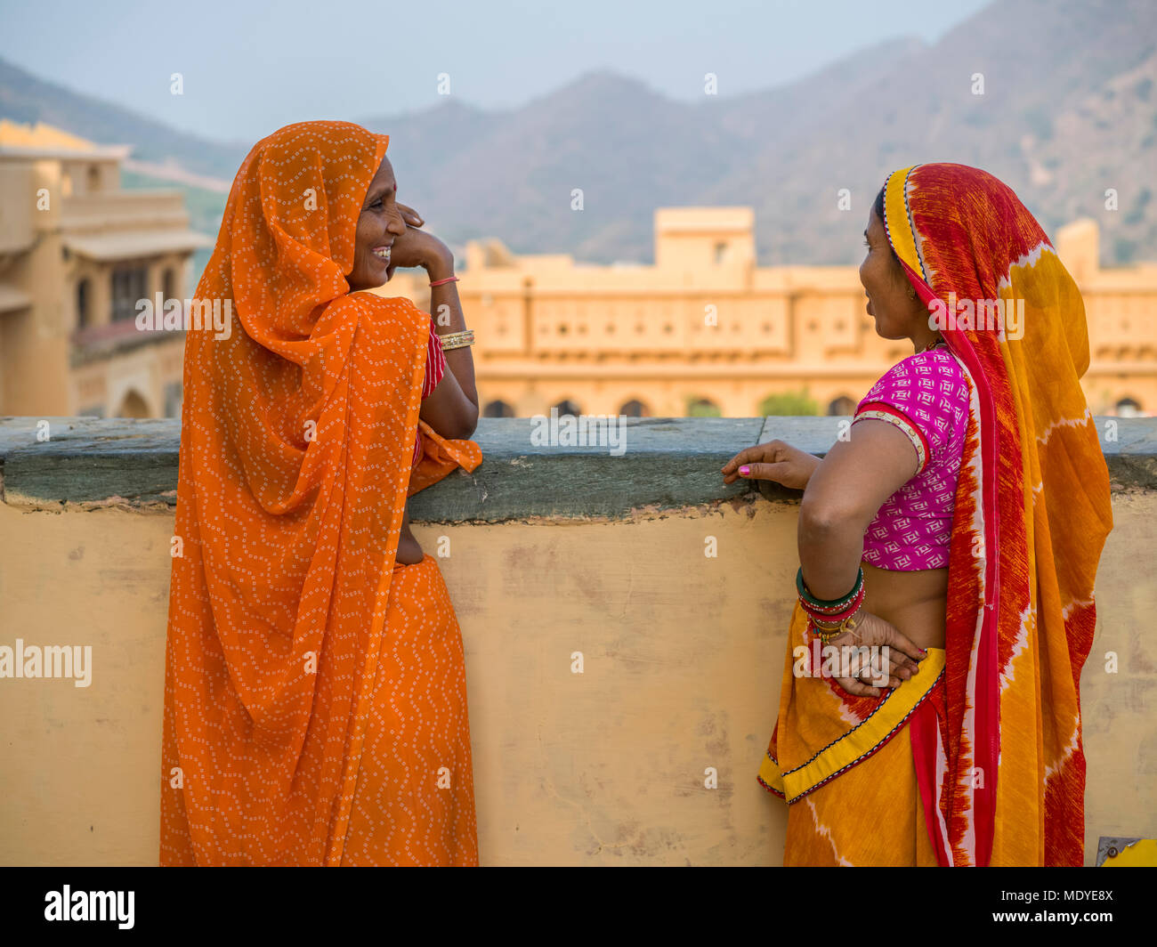 Two women in colourful traditional Indian clothing stand talking and looking out in Amer Fort; Jaipur, Rajasthan, India Stock Photo