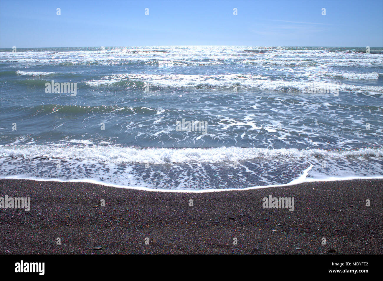 Atlantic ocean waves rolling onto an irish pebble beach with the afternoon sunlight glinting in the wave caps. West Cork beach holiday destination. Stock Photo