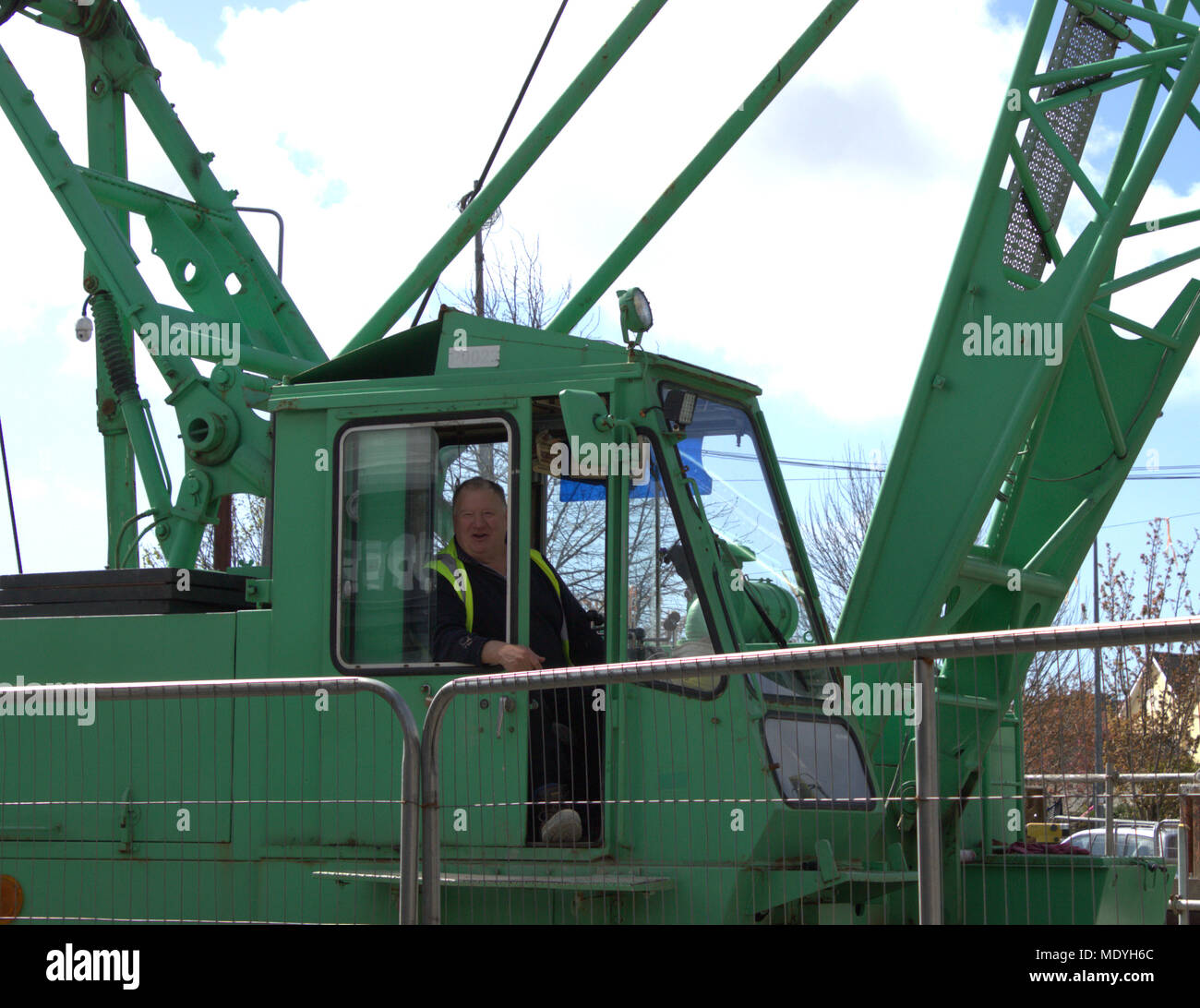 middle aged male crane driver in his cab talking to passers by while waiting for his load to be secured before lifting. Stock Photo
