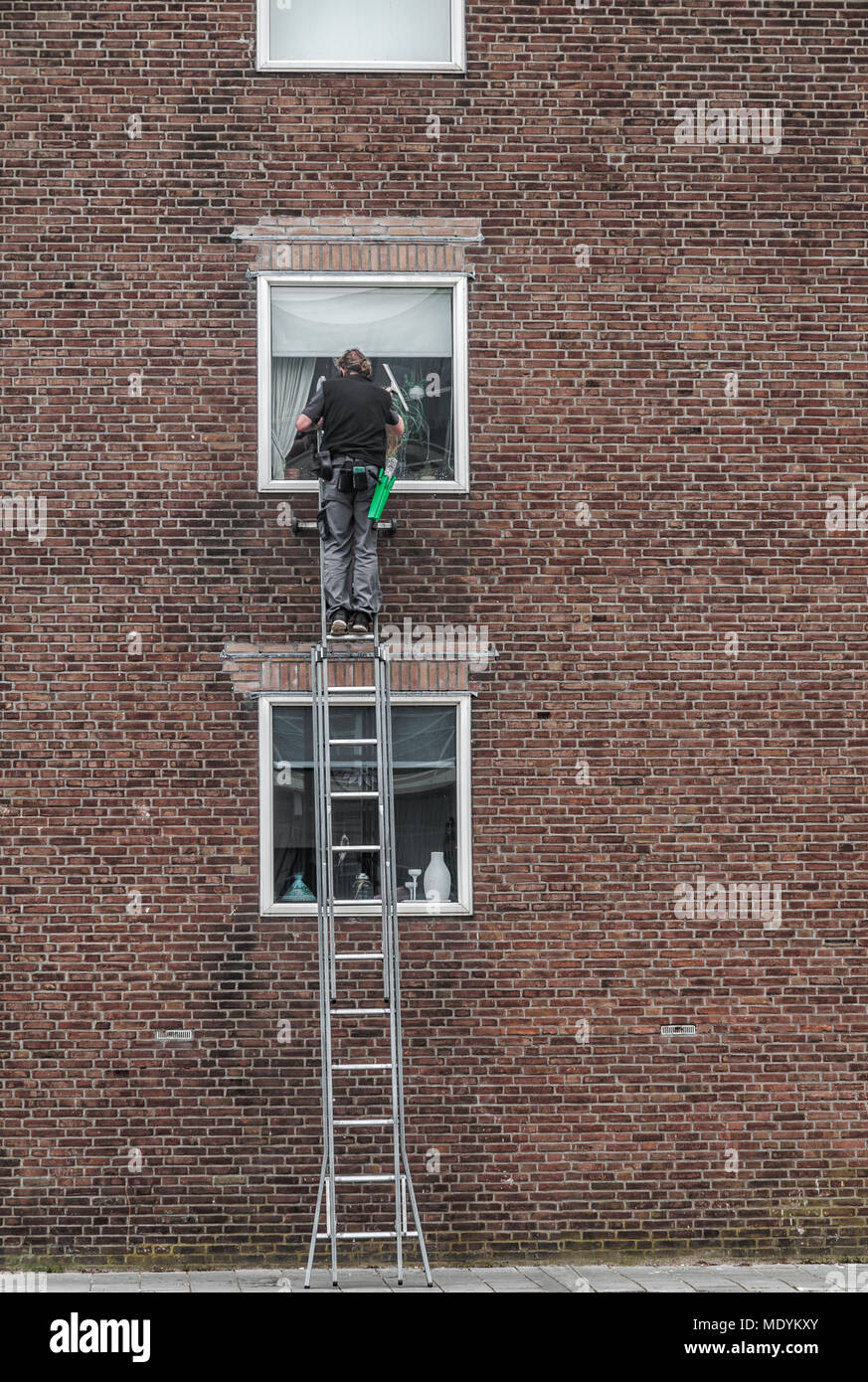 window cleaner is high on a ladder to wash a window of an apartment