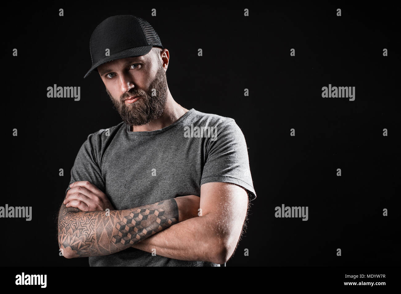 Pensive Black bearded male dressed in a grey shirt, sunglasses and baseball cap. Stock Photo