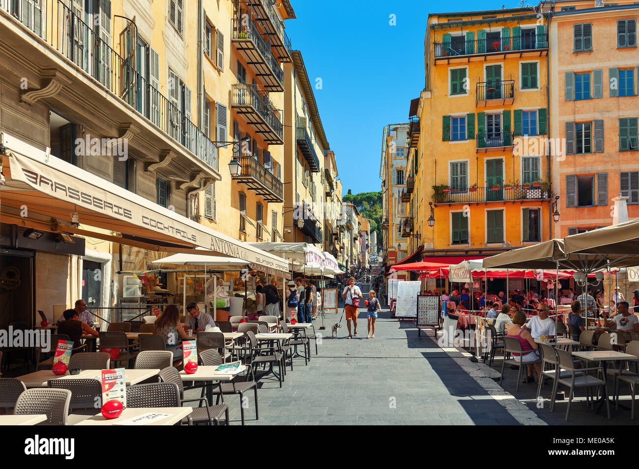 People sitting in outdoor restaurants on narrow street in Old town of Nice -  fifth most populous city in France. Stock Photo