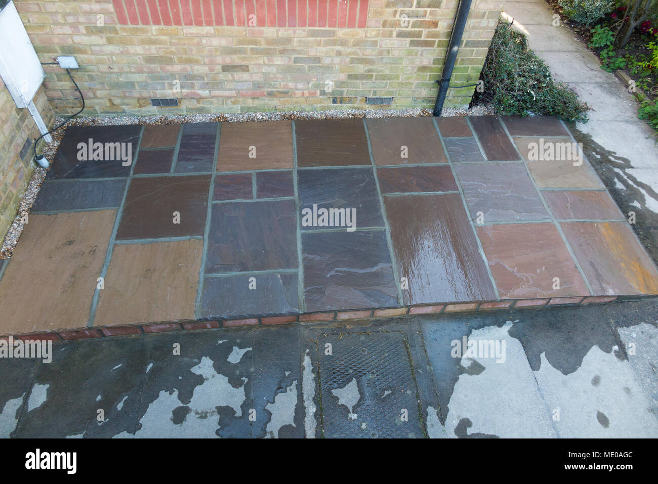A new patio made with stone slabs, with water on it to wet the drying mortar / cement as it cures – dries – built in the front garden of a small house Stock Photo