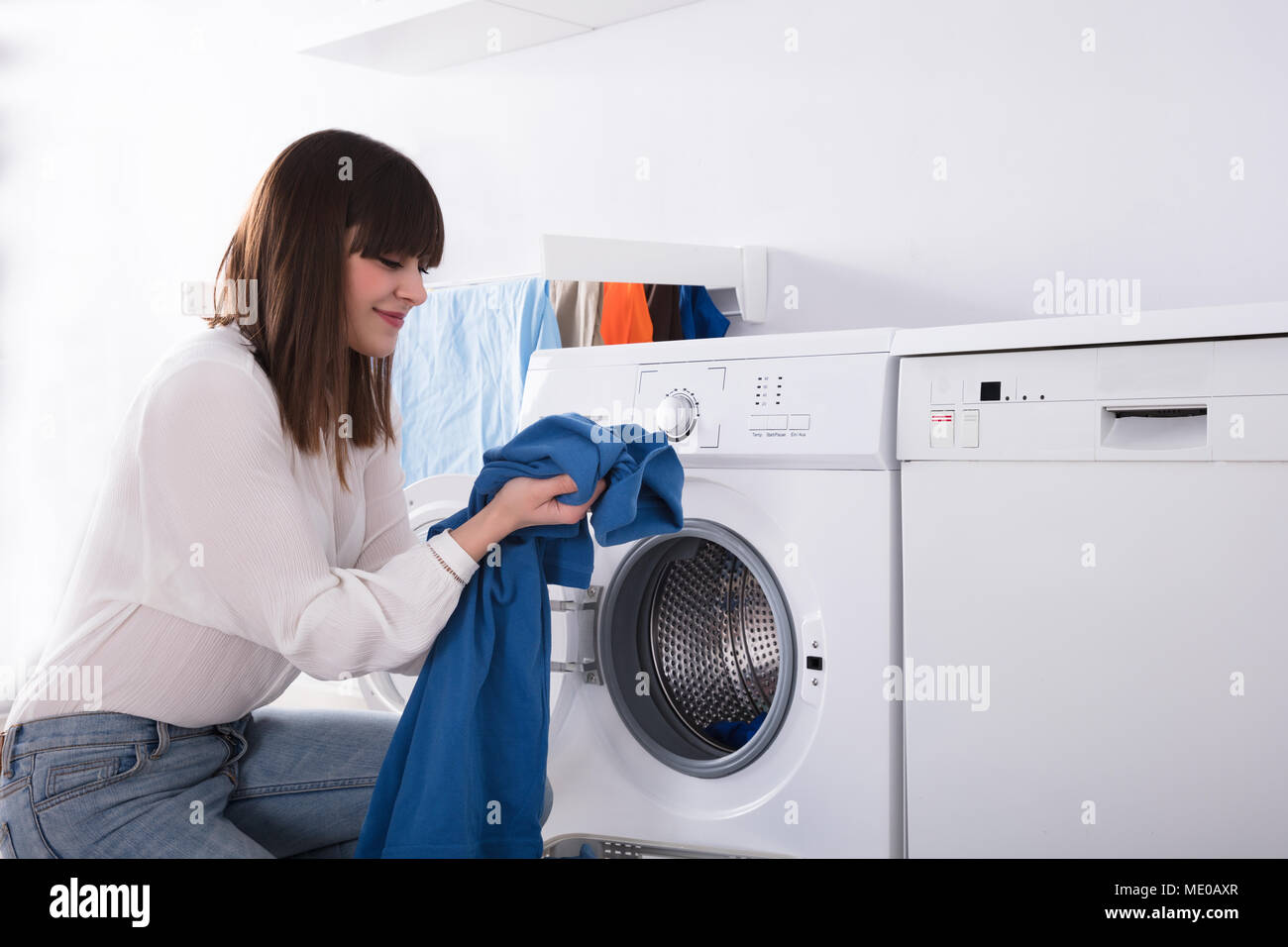 Young Woman Smelling Blue Cloth After Washing In Washing Machine Stock Photo