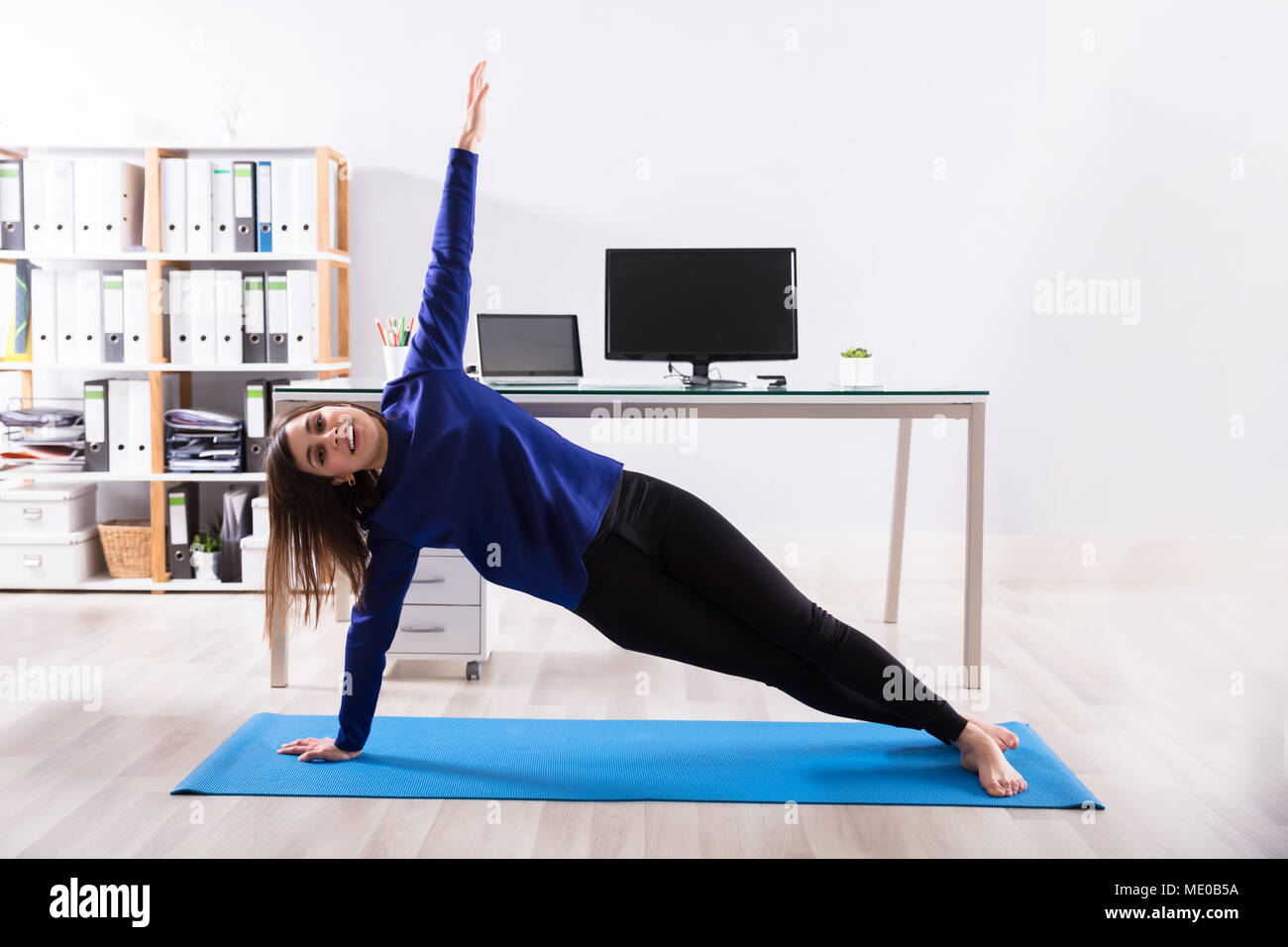 Young Businesswoman Doing Stretching Exercise On Exercise Mat At Workplace Stock Photo