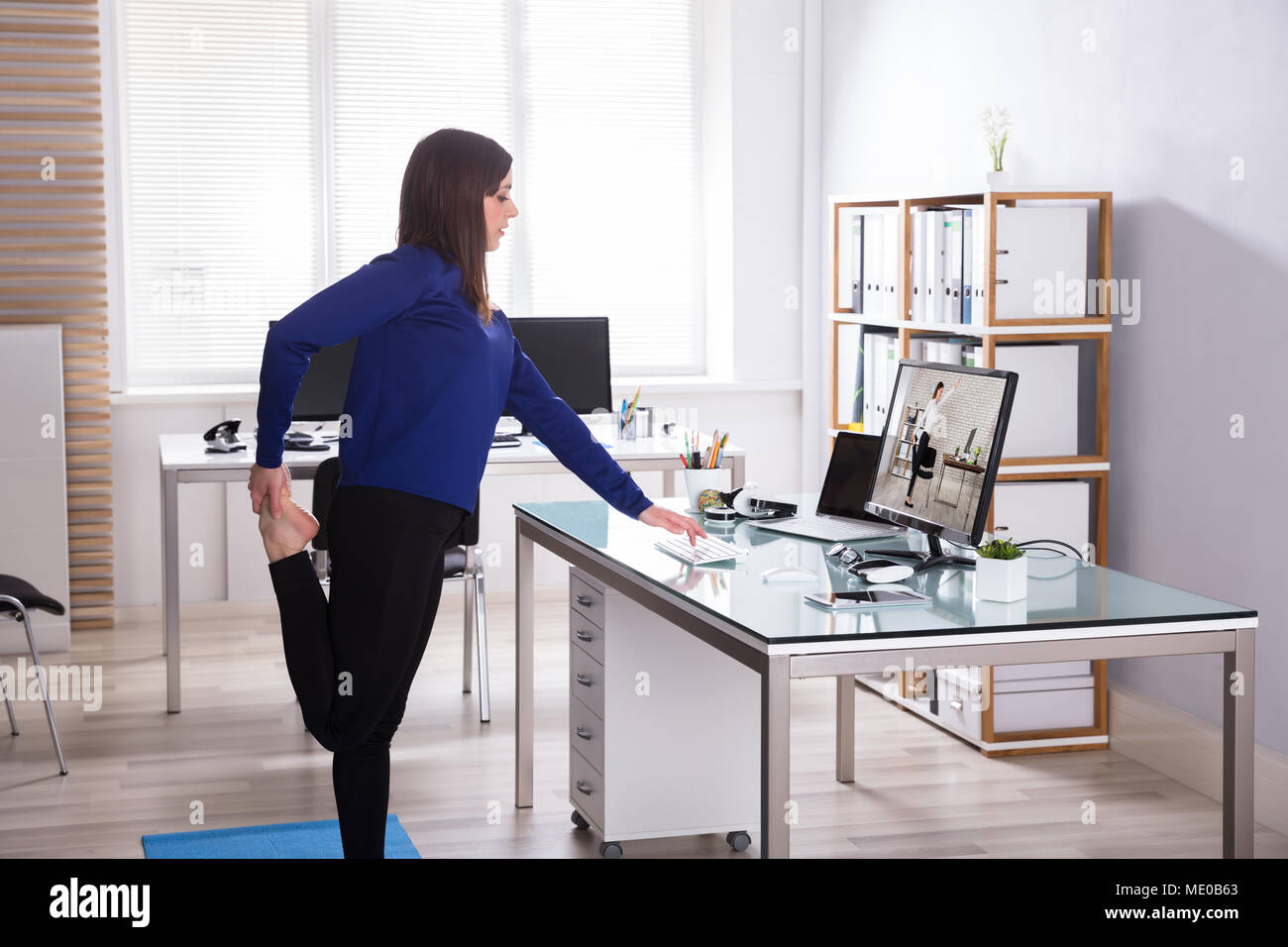 Young Businesswoman Looking At Invoice On Computer Doing Yoga Stock Photo