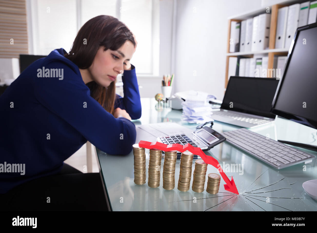 Red Arrow Over Decreasing Stacked Coins Showing Downward Direction In Front Of Upset Businesswoman Stock Photo