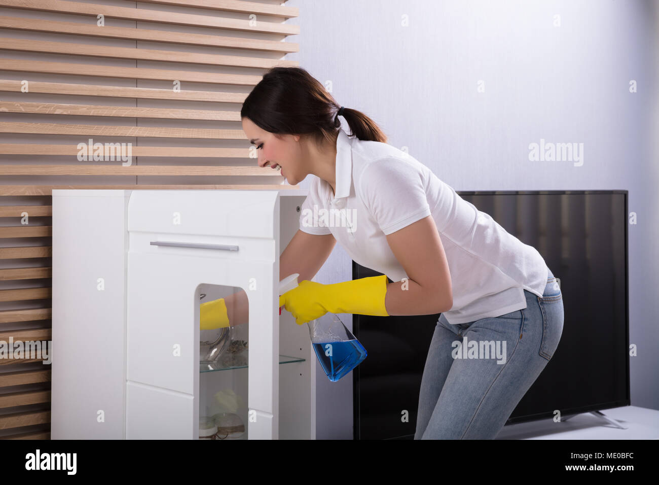 Portrait Of A Smiling Young Woman Cleaning Furniture With Spray Stock Photo