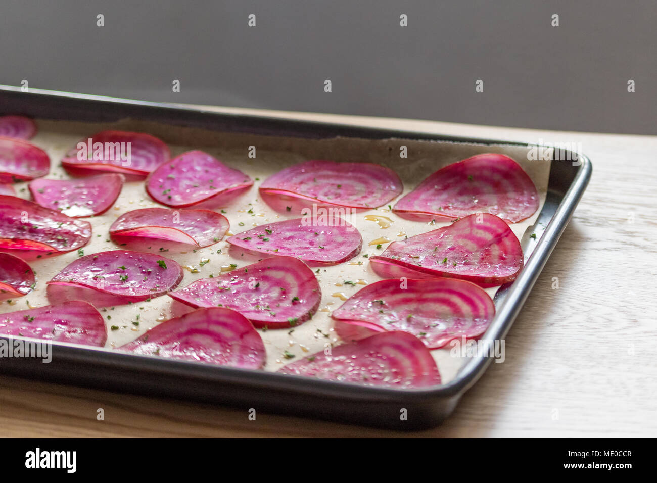 Slices of candy beetroot (chioggia beets) on a lined baking tray, ready for making oven-baked veggie chips. Stock Photo