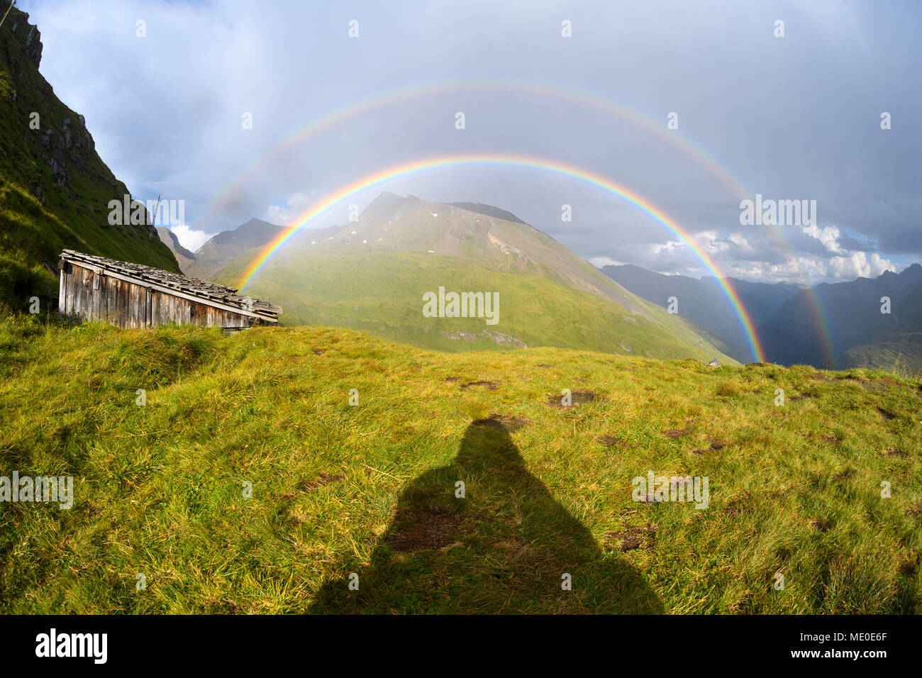 Shadow of a man looking at rainbow over mountains at Kaiser Franz Josefs Hohe in Hohe Tauern National Park, Carinthia, Austria Stock Photo