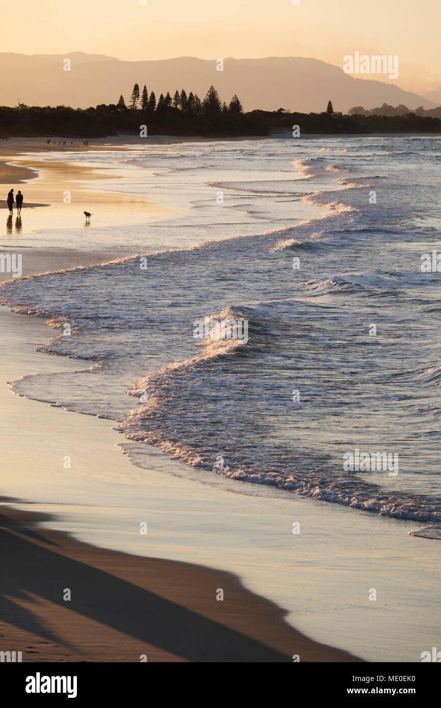 Silhouette of people walking along beach with pastel waves hitting shoreline at Byron Bay in New South Wales, Australia Stock Photo