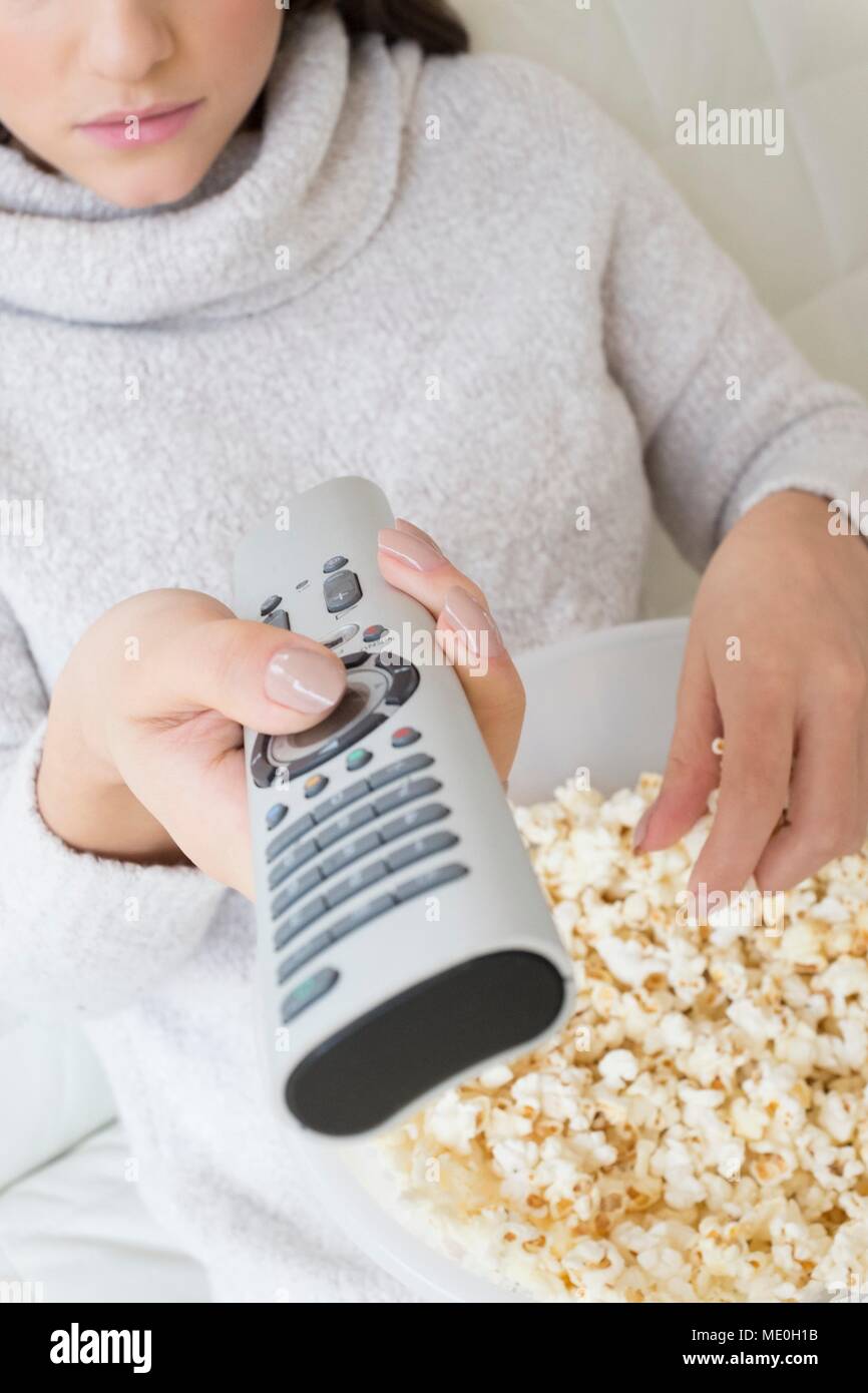 Young woman with tv remote eating popcorn, close up. Stock Photo