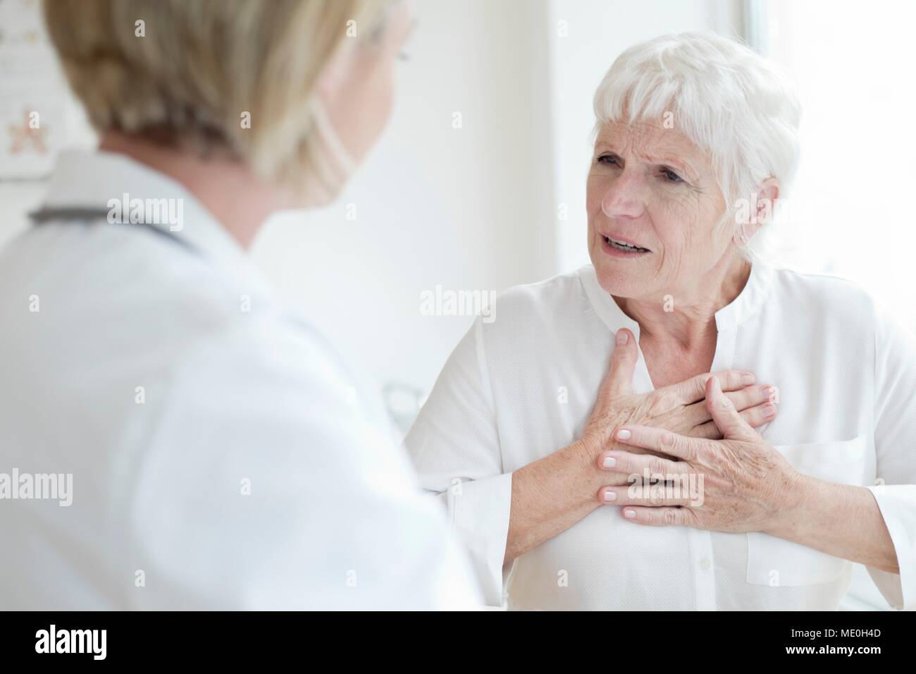 Senior woman touching chest and talking to female doctor. Stock Photo