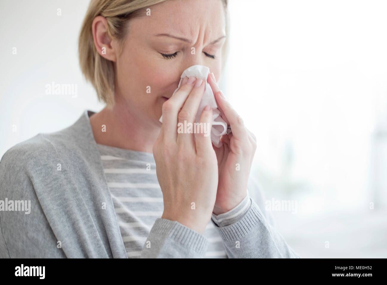 Mid adult woman blowing her nose. Stock Photo