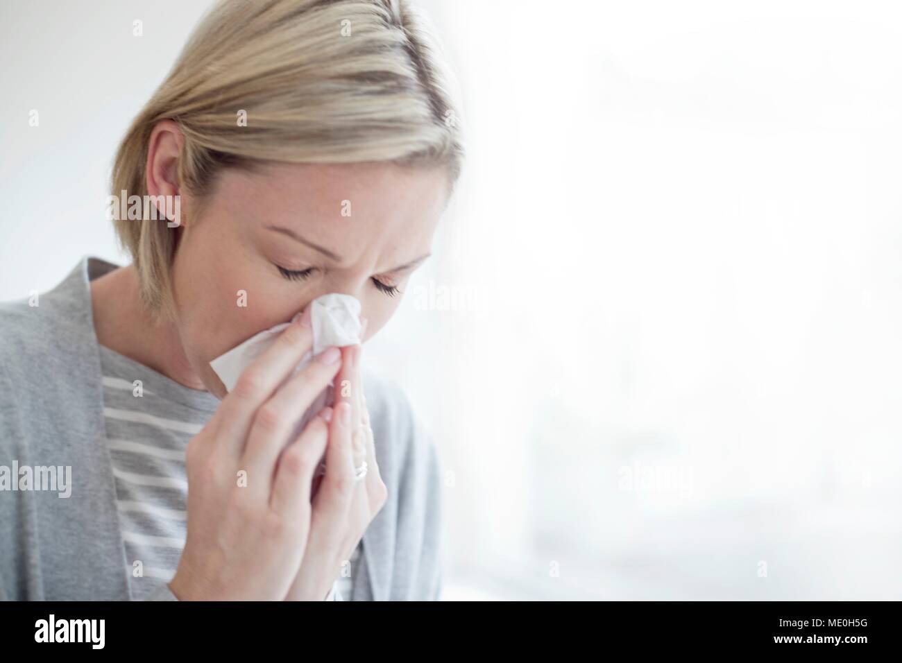 Mid adult woman blowing her nose. Stock Photo