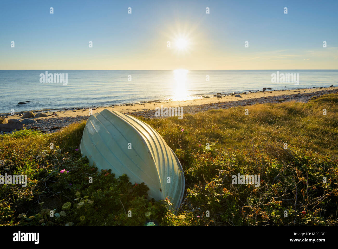 Small boat upside down on beach at sunset in summer at Sealand Odde in Odsherred on the Baltic Sea in Sealand, Denmark Stock Photo