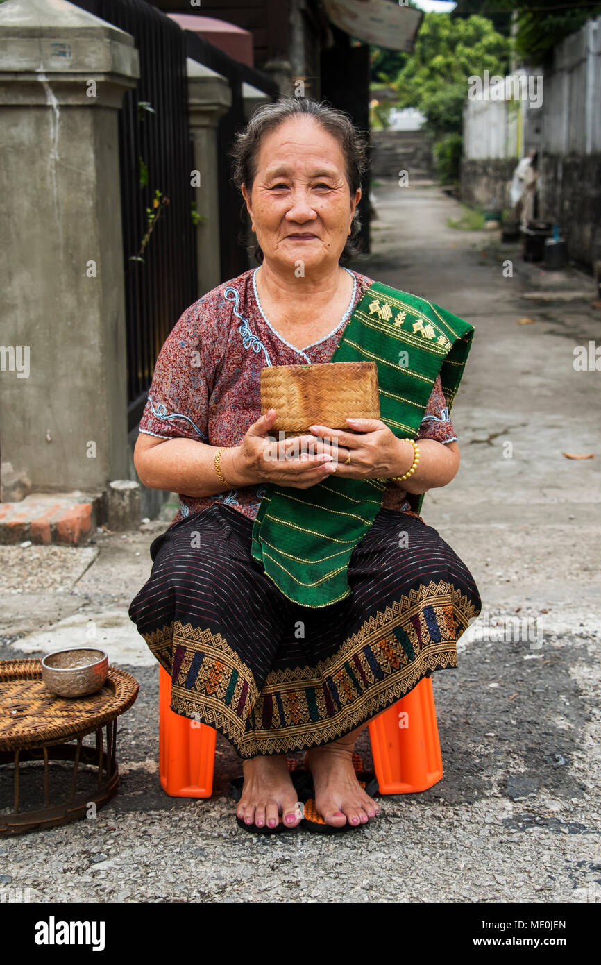 Woman waiting to give Buddhist monks alms on Khounsua Road at dawn; Luang Prabang, Luang Prabang, Laos Stock Photo