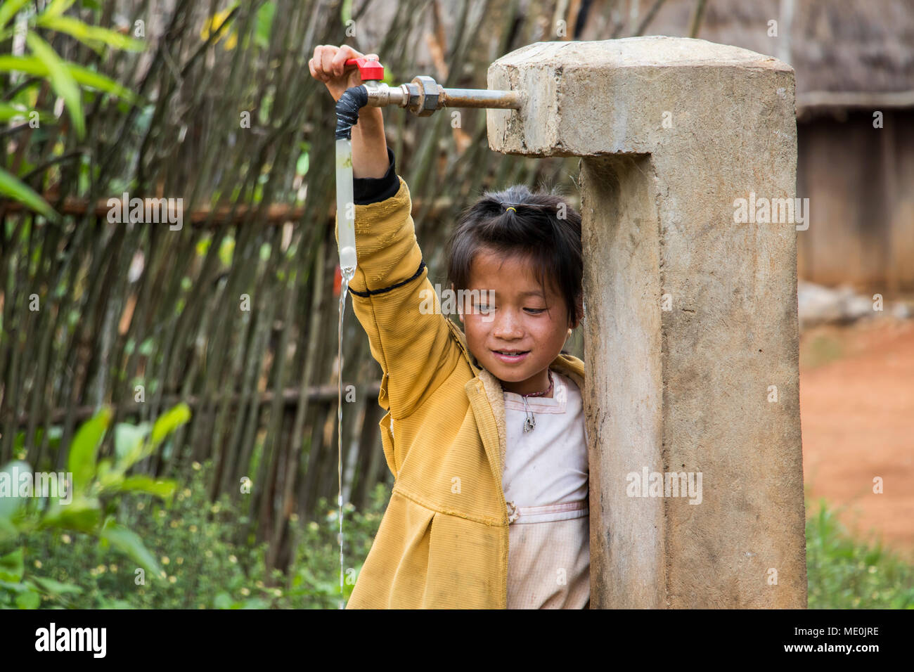 Hmong girl playing with a water tap in Na Kam Peng, also called Bomb Village, Xiangkhouang, Laos Stock Photo