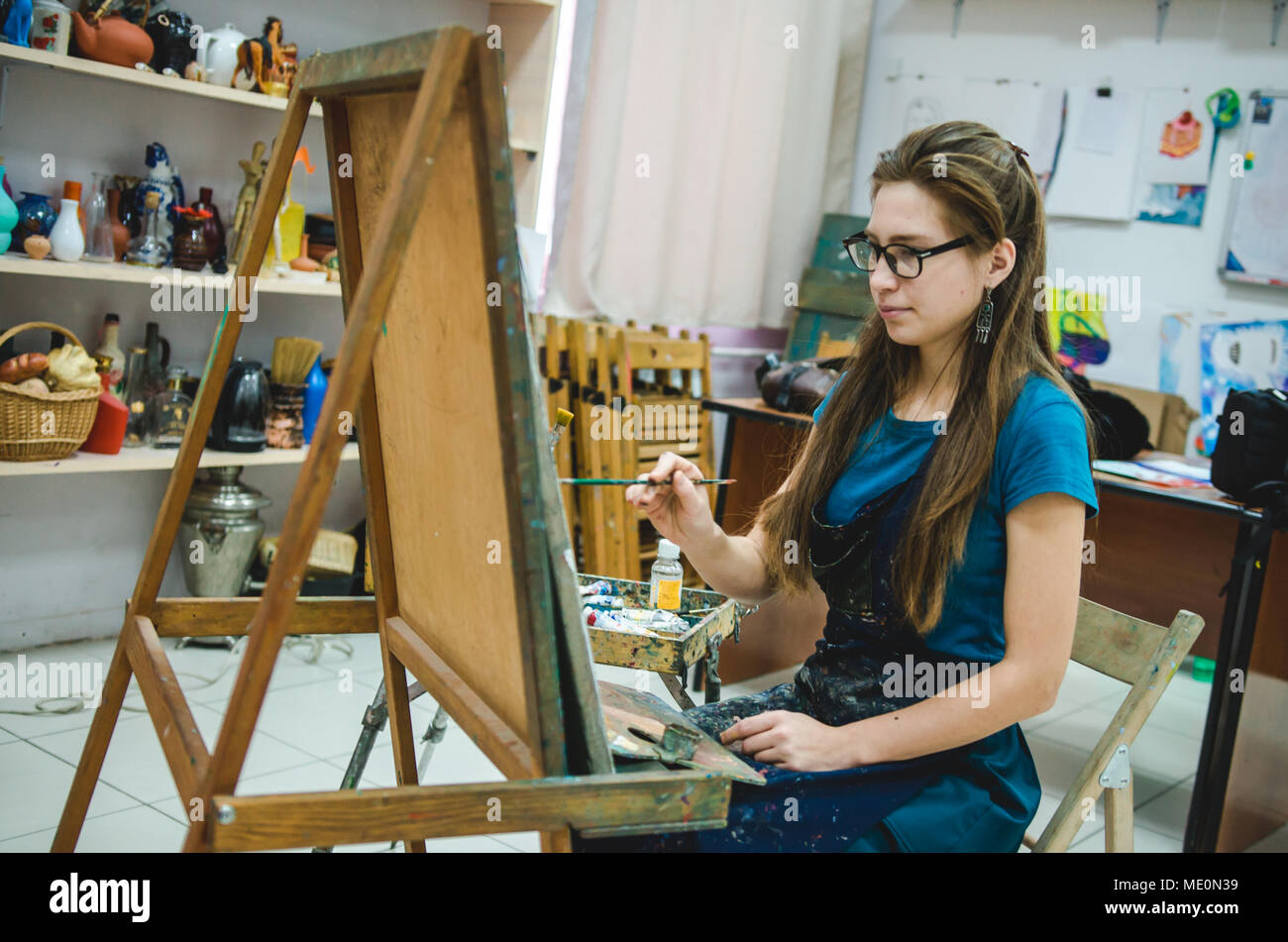Pretty female artist drawing on easel while sitting in art studio Stock ...