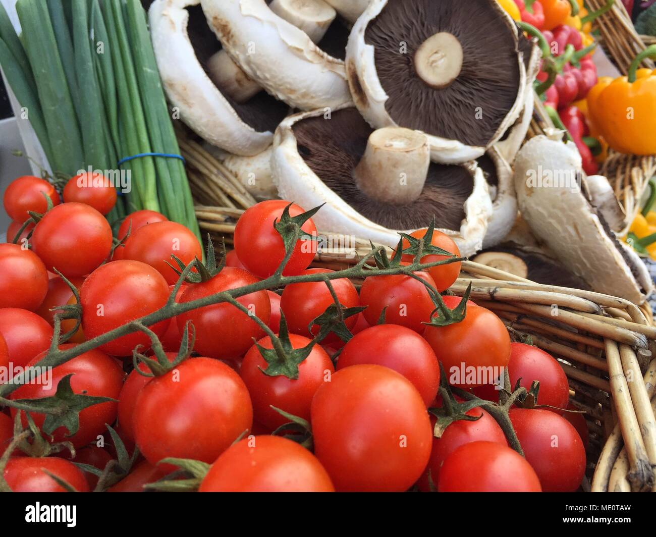 An outdoor market stall laden with a variety of fresh, organic fruit and vegetables including tomatoes, mushrooms and peppers. Stock Photo