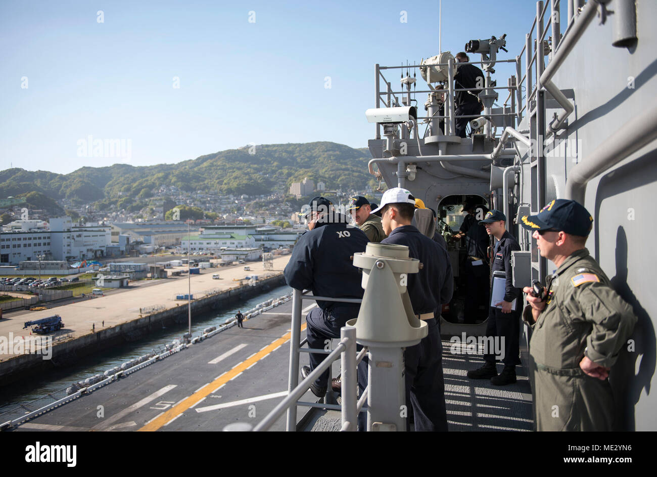 180418-N-WF272-218 SASEBO, Japan (April 18, 2018) Capt. Larry McCullen, center, commanding officer of the amphibious assault ship USS Bonhomme Richard (LHD 6), Capt. Richard Lebron, executive officer, and bridge officers observe pier operations as the ship departs Sasebo, Japan for the last time. Bonhomme Richard has been the flagship of the Amphibious Force 7th Fleet since April 2012 and will now transit to its new homeport in San Diego for follow-on operations and eventual upgrades to become F-35B Lightning II capable. (U.S. Navy photo by Mass Communication Specialist 2nd Class Diana Quinlan Stock Photo