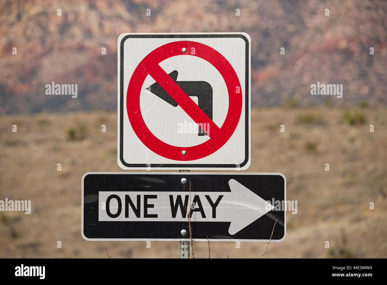 one way and no left turn signs in red black and white with out of focus mountains behind Stock Photo