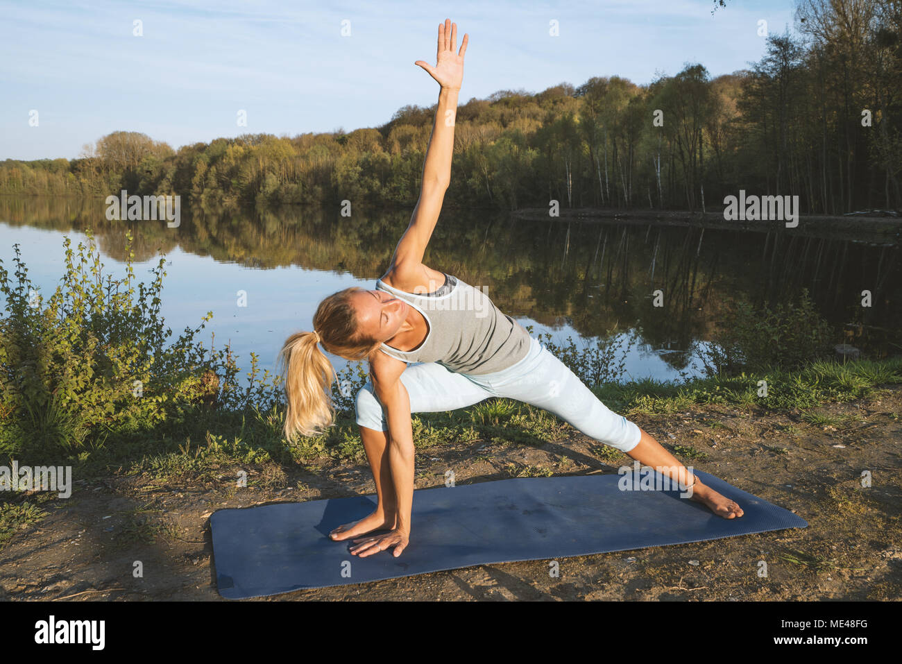 Young woman exercising yoga by the lake at sunset, people travel nature wellbeing and relaxation concept. Shot in France, Europe. Stock Photo