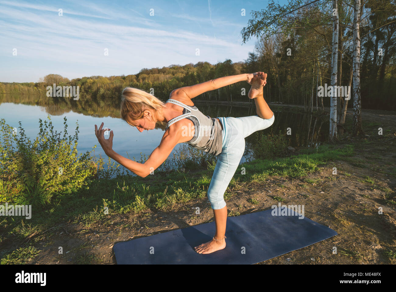 Young woman exercising yoga by the lake at sunset, people travel nature wellbeing and relaxation concept. Shot in France, Europe. Dancer pose Stock Photo